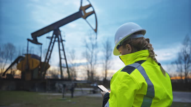 SLO MO Female engineer uses her smartphone while she observes the operation of a pumpjack