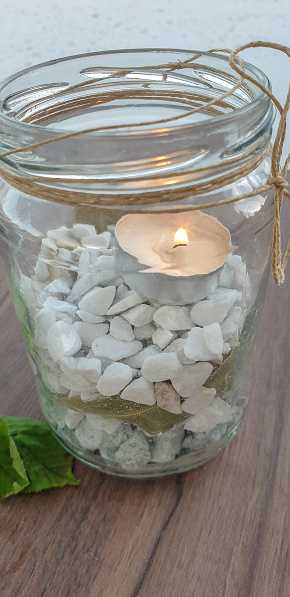 Small candle in jar filled with stones on table