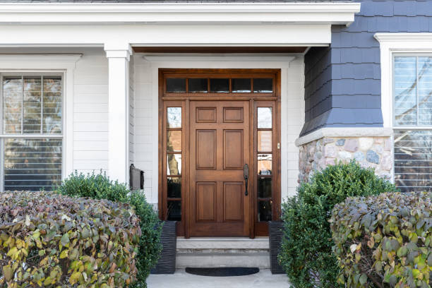 A blue house with a wooden front door. A wooden front door, surrounded by windows, with white, blue, and stone siding. blue front door stock pictures, royalty-free photos & images