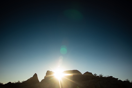 lens flare brings a dramatic feel to an abstract landscape of clear blue sky and silhouetted mountain ridge.  copy space.  such beautiful and austere, minimalist nature can be found in the sandia mountains of albuquerque, new mexico.