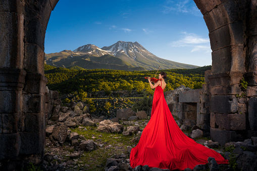 Young woman playing the violin in a red long dress. mountain landscape