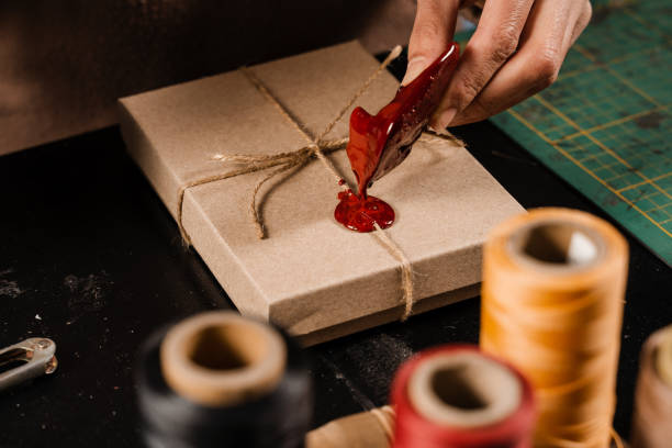 istock Process of sealing waxing on gift packaging in workshop. Craftsman is burning sealing wax and applying on craft present. 1456438545