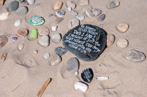 Dennis, Massachusetts, USA- March 12, 2021-  Smooth rocks on a sandy beach on Cape Cod have been hand transformed into works of inspiration and encouragement during troubling times.