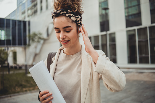 One young woman, Portrait of a young woman, student or designer, standing next to an office building or college and holding blueprint papers in her hands