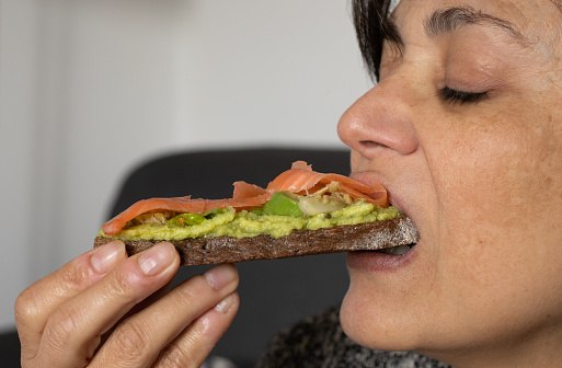 woman eating whole wheat toast with avocado and smoked salmon.