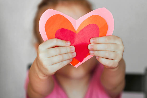 Hobby, art concept, DIY gift for Valentine's Day DIY holiday card with a red paper heart, a symbol of love. child holding homemade paper cut hearts Mother's Day, Valentine's Day be my valentine stock pictures, royalty-free photos & images