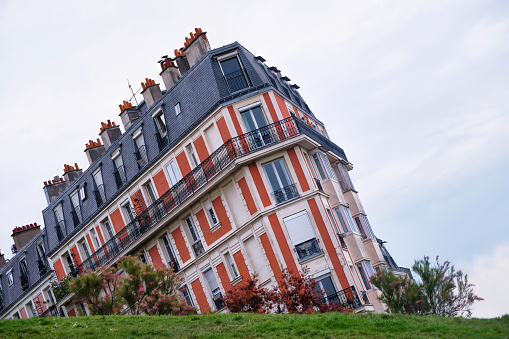 Paris, France - May, 2022: A 19th century parisian brick apartment building with a grassy slope in the foreground.
