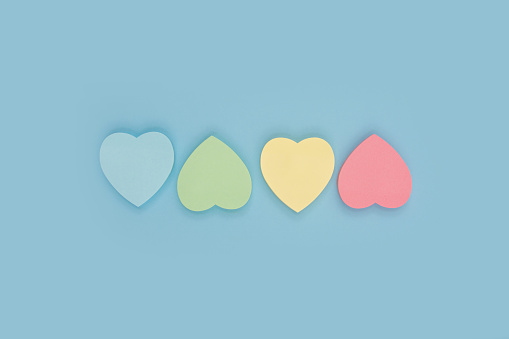 Collection of different heart pastel colored sheets of note papers ready for your message on blue background. Top view. Close up. Sticky notes.