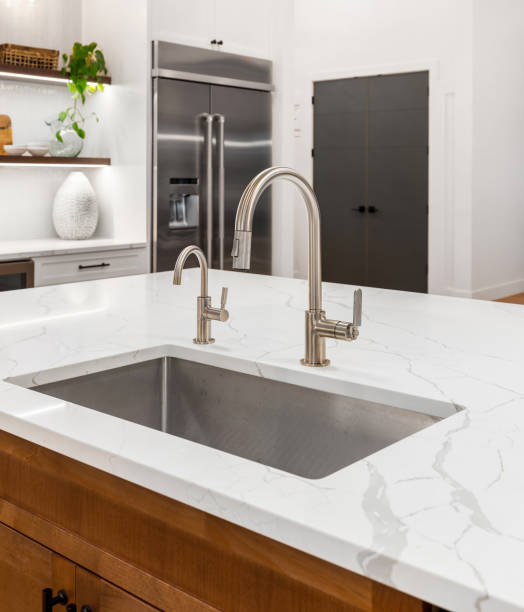 kitchen detail in new luxury home with stainless steel undermount sink and quartz island. Stainless steel refrigerator and floating shelves in background. stock photo