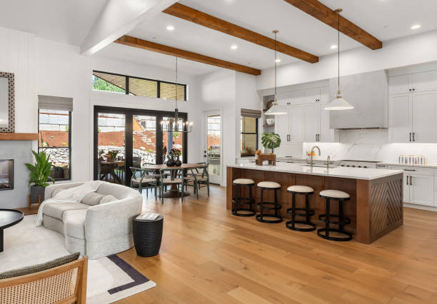 ruang tamu dan dapur yang indah di rumah mewah baru dengan lemari putih, balok kayu, lampu gantung, dan lantai kayu keras - modern living room potret stok, foto, & gambar bebas royalti