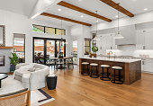 Beautiful living room and kitchen in new luxury home with white cabinets, wood beams, pendant lights and hardwood floors