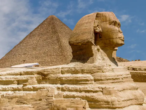 Sculpture of the Great Sphinx against the blue sky. Profile view. The head, part of the body and the top of the ancient pyramid above the back are visible. Egypt. Giza