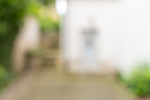 Blurry house with stairs and green plants as background. White facade in the backyard with an empty copy space in front. Defocused outdoor area.