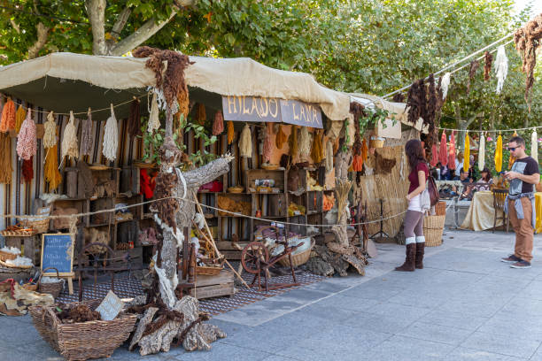 tourists looking at an outdoor shop of wools dyed with natural dyes and several pedal wooden spinning wheels and other handicraft tools Alcala de Henares, Madrid, SPAIN - October 10, 2016:  tourists looking at an outdoor shop of wools dyed with natural dyes and several pedal wooden spinning wheels. taken during the celebration of a medieval festival in the streets of the city alcala de henares stock pictures, royalty-free photos & images