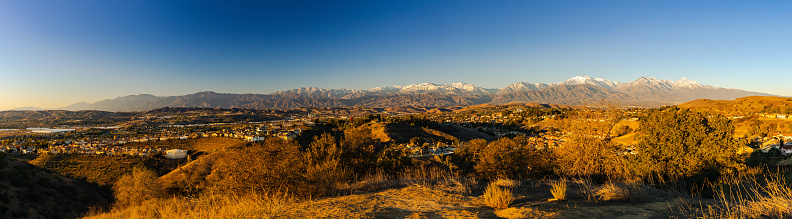 This January 2022 panoramic sunset photo shows a skyline view of Diamond Bar, California, United States. In the foreground are residential neighborhoods in Diamond Bar. On the left are large commercial buildings in the City of Industry. In the center distance are the cities of Walnut and Pomona. In the background are the snow-capped San Gabriel Mountains including Mount Wilson on the far left to Mount Baldy on the far right. This image was taken from the trails near the Diamond Bar Center. An extended drought in the region has left a parched landscape.