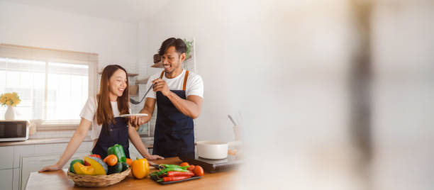 istock Happy young asia couple cooking together with vegetables in cozy kitchen, practicing vegetarian cooking together on vacation. First time cooking simple food tasting together love and valentine concept 1456475912