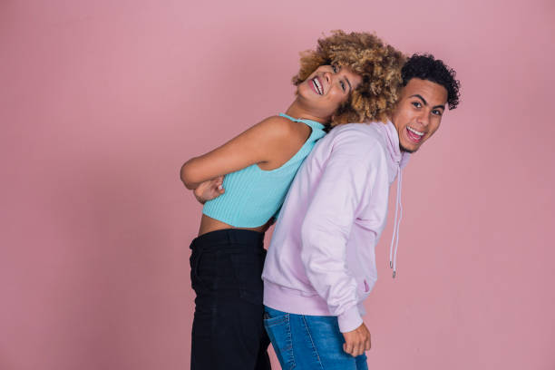 Couple of Latino friends from Bogota Colombia between the ages of 20-39 smiling and enjoying themselves while standing in pink studio background wearing casual clothing