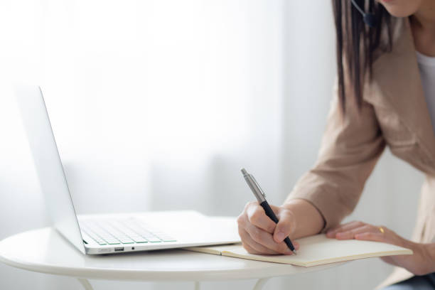 istock Closeup hands young asian woman writing on notebook for planning working and using laptop computer on desk at home, female notes about finance, female study, business and communication concept. 1456476607