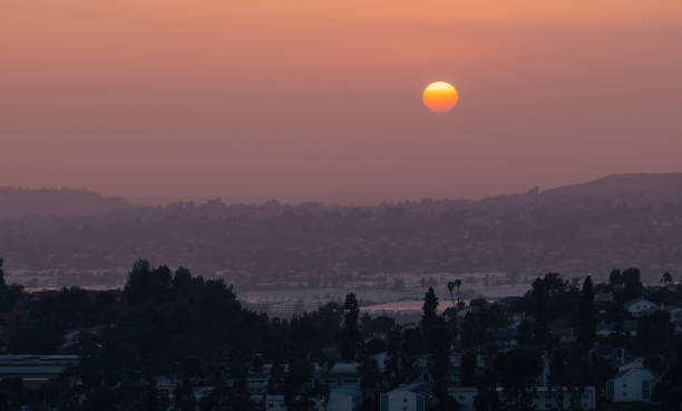 This May 2022 sunset photo shows a skyline view of Diamond Bar, California, United States. A thick layer of smog obscures the sun and the view of the San Gabriel Valley. The air pollution can lead to severe health consequences. This image was taken from near the Diamond Bar Center. In the foreground are residential neighborhoods in Diamond Bar.  In the near distance, center, large commercial buildings in the City of Industry.
