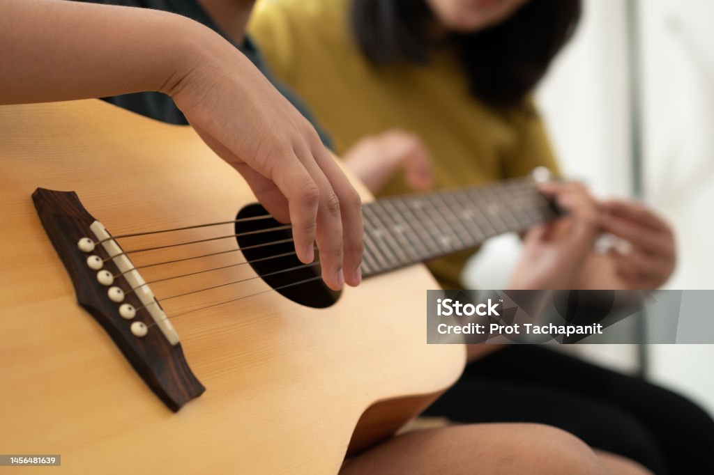 Asian boy playing guitar with mom in the living room for teaching him son play guitar, feel appreciated and encouraged. Concept of a happy family, learning and fun lifestyle, love family ties Guitar Stock Photo