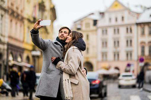 Happy young couple taking a selfie with smart phone in the city on winter day.