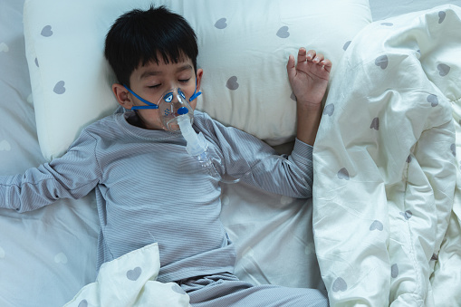 Sick Asian child boy Respiratory syncytial virus (RSV) wears a pediatric ventilator lying in bed at home. health and medical