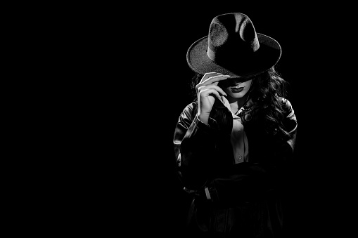 Silhouette: a female detective in a coat and hat . Dramatic noir portrait in the style of books and detective films of the 1950s. black and white snapshot.