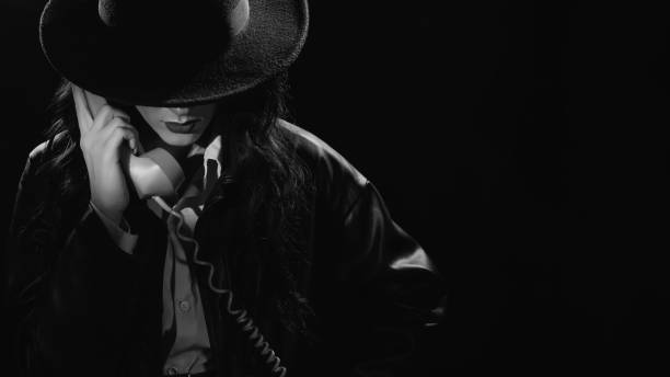 Dark noir portrait of a female detective holding a retro telephone receiver. Private detective, spy, investigation concept. black and white snapshot Dark noir portrait of a female detective holding a retro telephone receiver. Private detective, spy, investigation concept. black and white snapshot. film noir style stock pictures, royalty-free photos & images