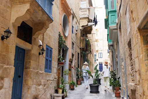 Back view of female friends walking in Mediterranean alley on sunny day