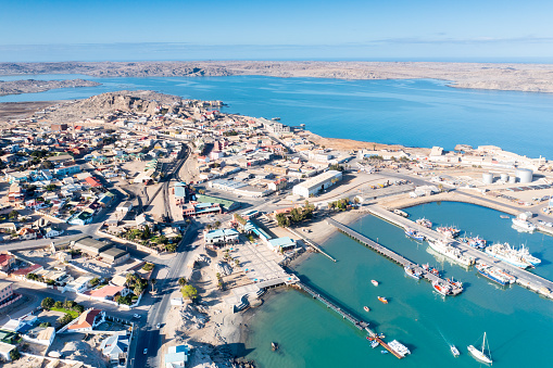 An aerial view of Luderitz harbour in Namibia. A commercial vessel is surrounded by fishing boats.