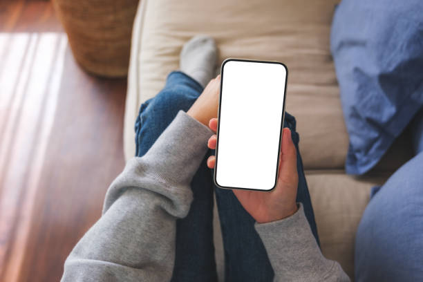 istock Top view mockup image of a woman holding mobile phone with blank desktop white screen while lying on a sofa at home 1456509597
