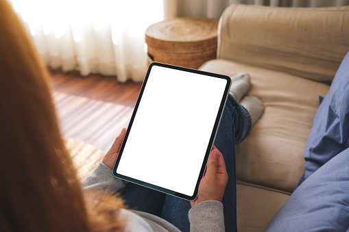 Mockup image of a woman holding digital tablet with blank desktop screen while lying on a sofa at home