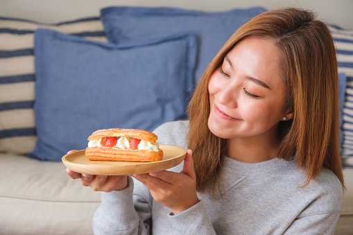 Portrait image of a woman holding a plate of strawberry Eclair