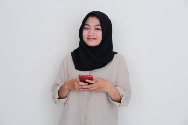 istock Young moslem women smiling at the camera while using her handphone 1456510898