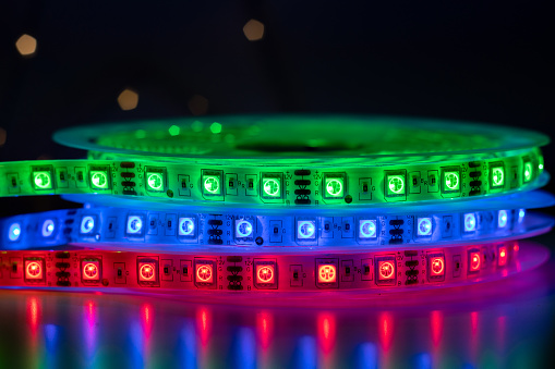 Bobbin with roll of glowing LED strip lighting placed on table, green, red and blue color