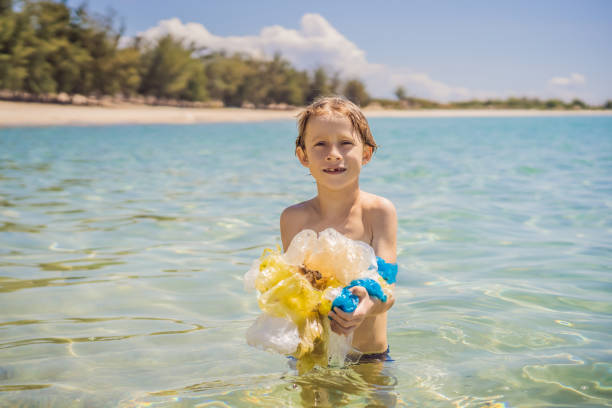 Boy collects packages from the beautiful turquoise sea. Paradise beach pollution. Problem of spilled rubbish trash garbage on the beach sand caused by man-made pollution and environmental, campaign to clean volunteer in concept.