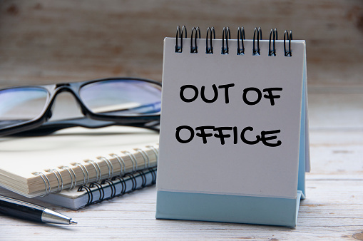 Out of office text on calendar desk with notebook and glasses background. Out of office concept