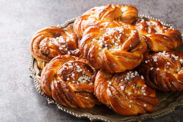 kanelbullar o kanelbulle è un tradizionale panini alla cannella svedese aromatizzati con spezie alla cannella e cardamomo e conditi con zucchero perlato in primo piano su un piatto. orizzontale - bun bread cake dinner foto e immagini stock