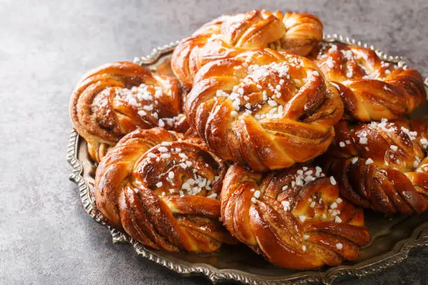 Kanelbullar or Kanelbulle is a traditional Swedish cinnamon buns flavored with cinnamon and cardamom spices and topped with pearl sugar close-up on a plate on the table. Horizontal