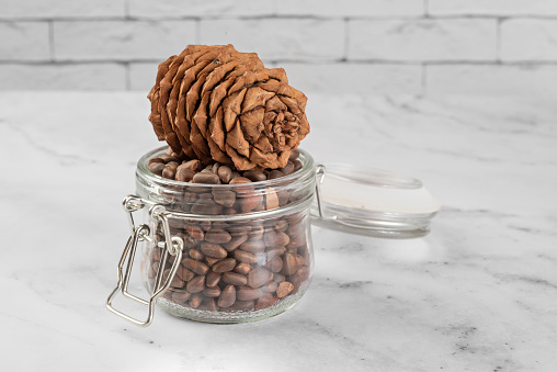 Pine nuts in a jar and a pine cone in the kitchen on a light background. The concept of organic food and protein food