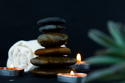 The art of stones with two burning candles and some flowers in black background used for relaxing concepts as yoga, massage and peaces concept of wallpaper design.