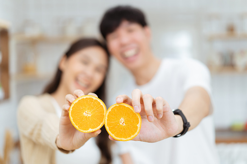 Happy cheerful Asian man and woman showing a half round of a fresh orange fruit to camera together and smiling.