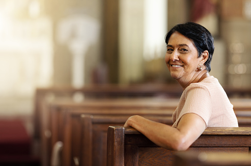 Senior woman, christian and happy in church, spiritual and religion after service, smile and lifestyle. Elderly female smile, portrait and empowerment while sitting in wood bench in catholic chapel