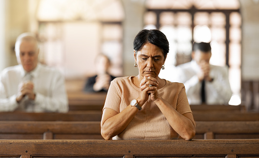 Faith, woman and praying in church, religion and spiritual connect, communication or believe. Senior female, mature lady or prayer in chapel with congregation, worship or trust with gratitude or hope
