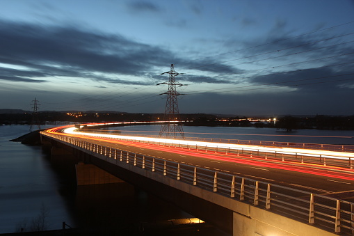 Long exposure of traffic light trails over new Carrington Bridge in Worcester evening time with flooded fields in background