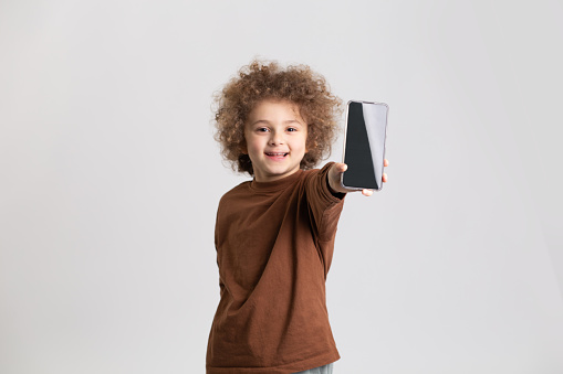 Studio shot of a young boy showing his phone to the camera