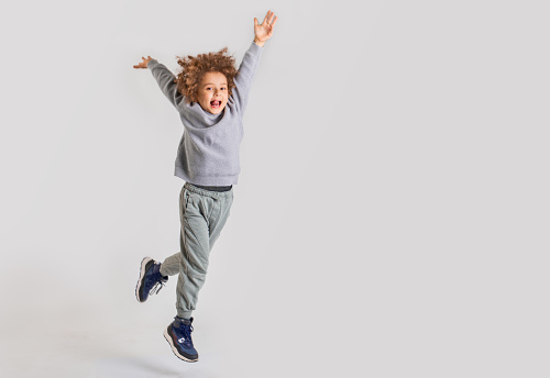 Joyful boy with curly hair jumping in the air for a studio photoshoot.