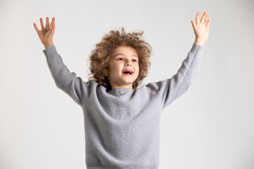 Joyful boy with curly hair jumping in the air for a studio photoshoot.