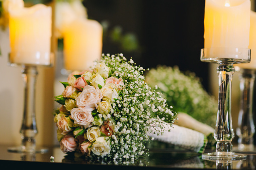 Wedding table with bouquet of white roses and burning candle .