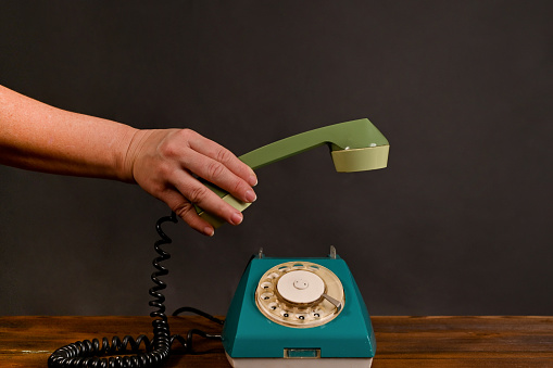 a woman's hand puts down the receiver of an old vintage phone.